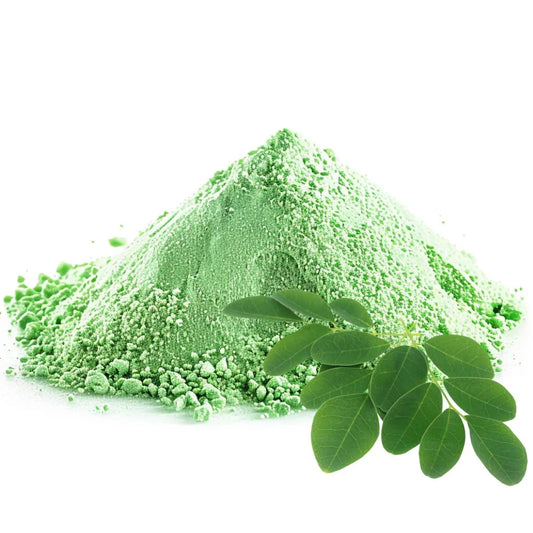 Moringa leaf powder heaped in a pile, accompanied by fresh green moringa leaves, isolated on a white background - WowNutri